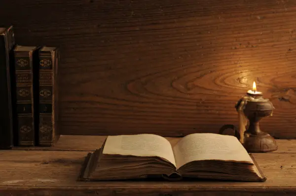 old book on a wooden table by candlelight