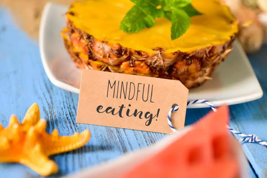 a brown paper label with the text mindful eating in front of some slices of pineapple and a piece of watermelon on a blue rustic wooden table
