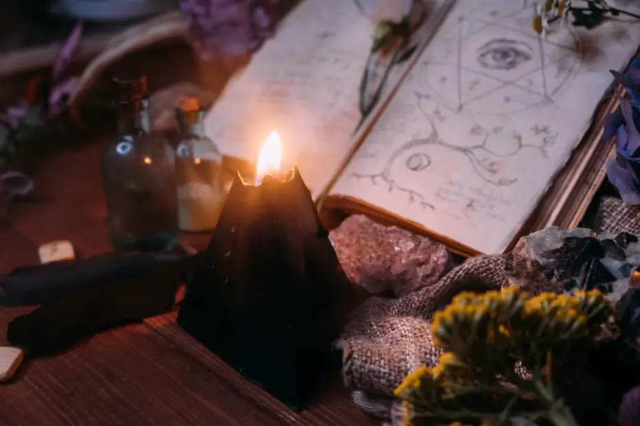 Open old book with magic spells, runes, black candle and herbs on witch table.